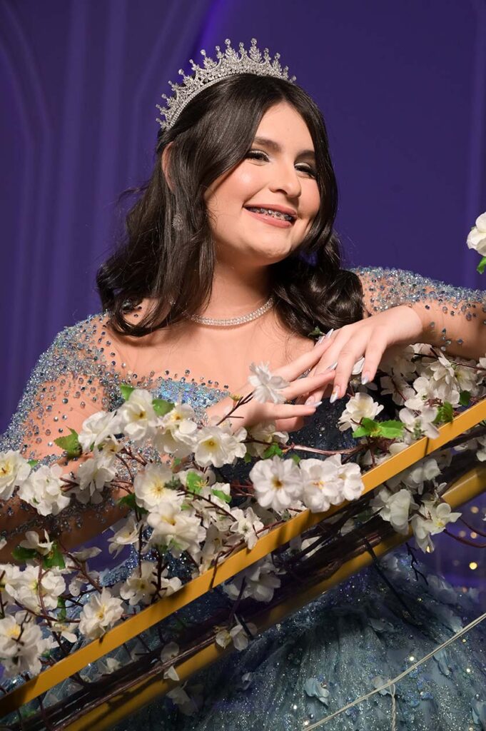 Debutante em vestido azul apoiada no corrimão entre flores brancas
