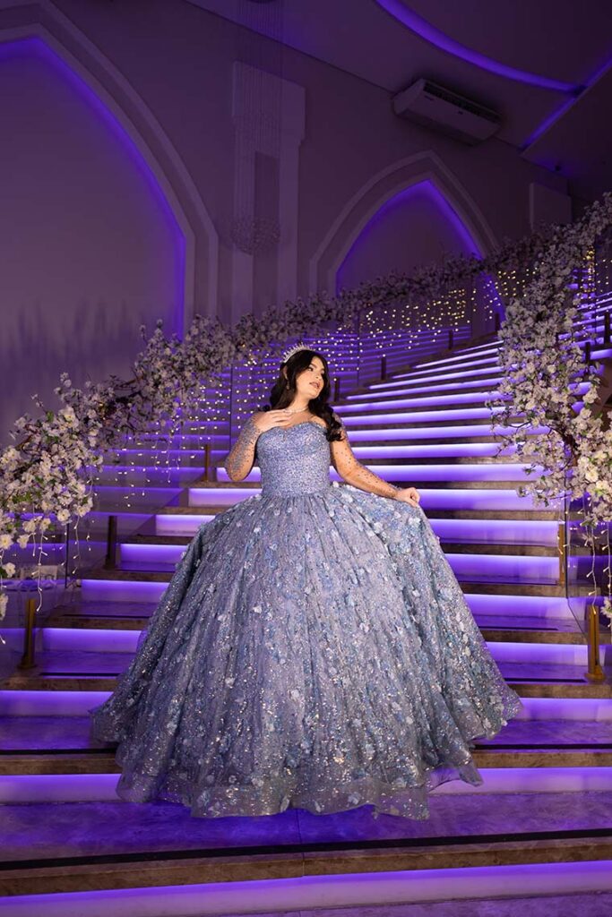 Debutante em vestido azul na escadaria iluminada em roxo
