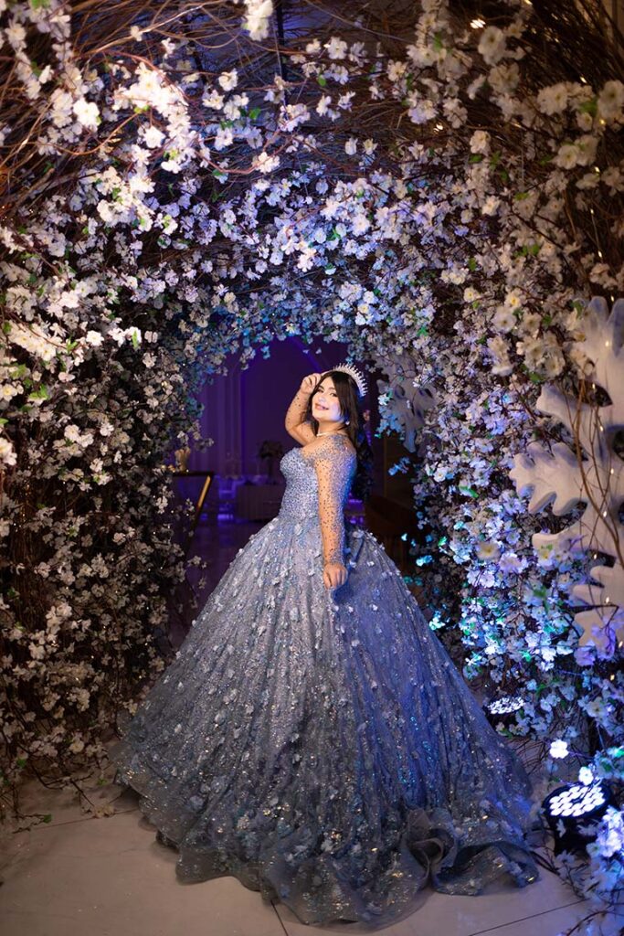 Debutante em vestido azul diante da parede de flores brancas