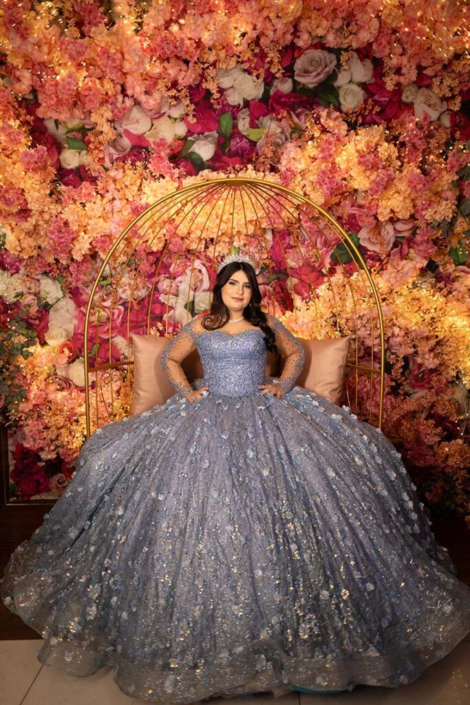 Debutante em vestido azul diante do arco de flores em tons de laranja