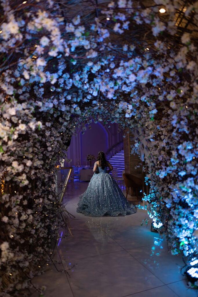 Debutante em vestido azul sob o arco de flores azuis e brancas
