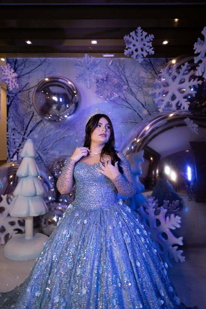 Debutante em vestido azul entre flocos de neve e pinheiros decorativos