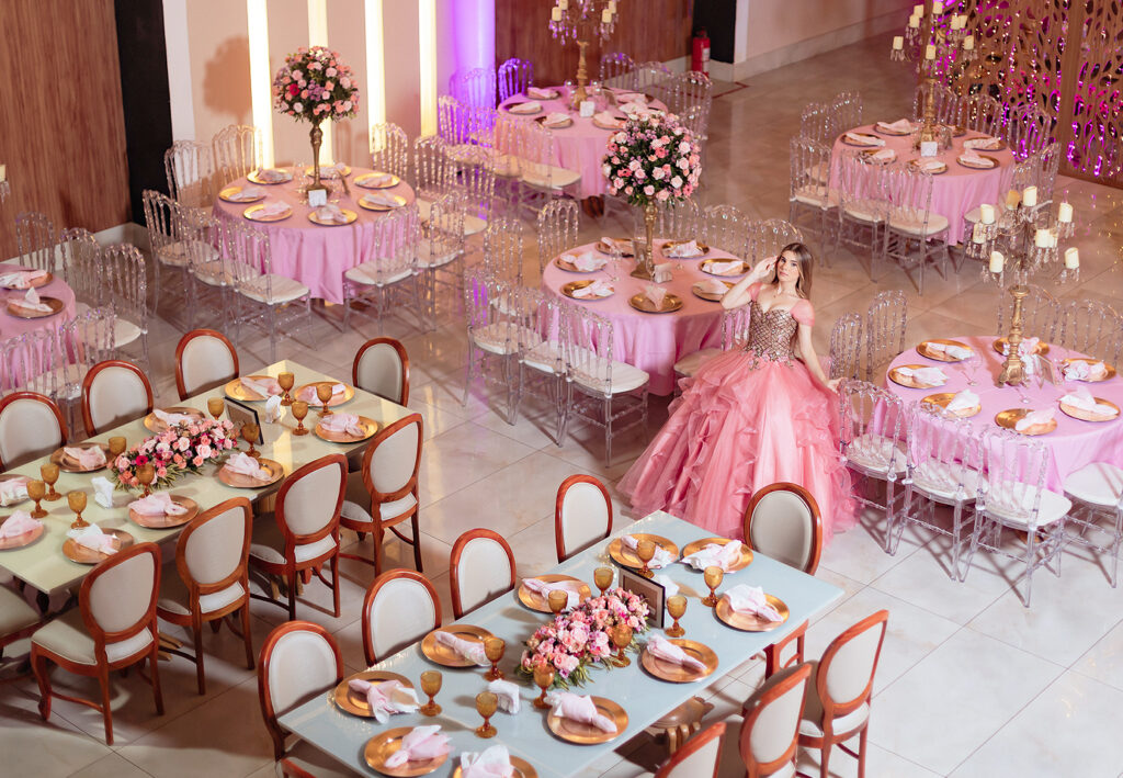 Debutante em vestido rosa no salão montado com mesas decoradas