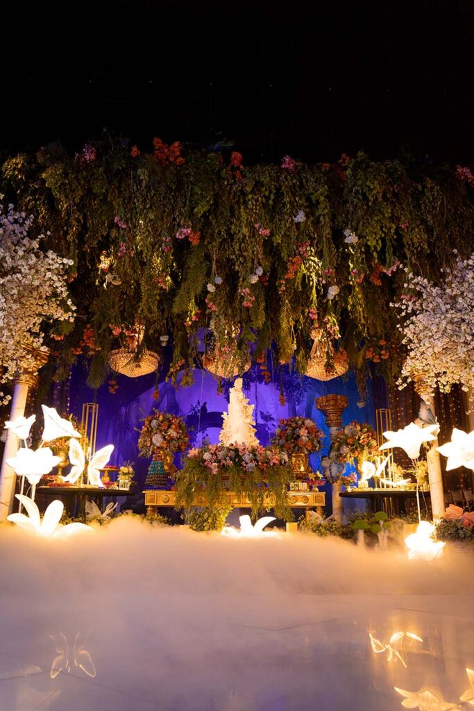 Cenário iluminado com flores suspensas e efeito de fumaça