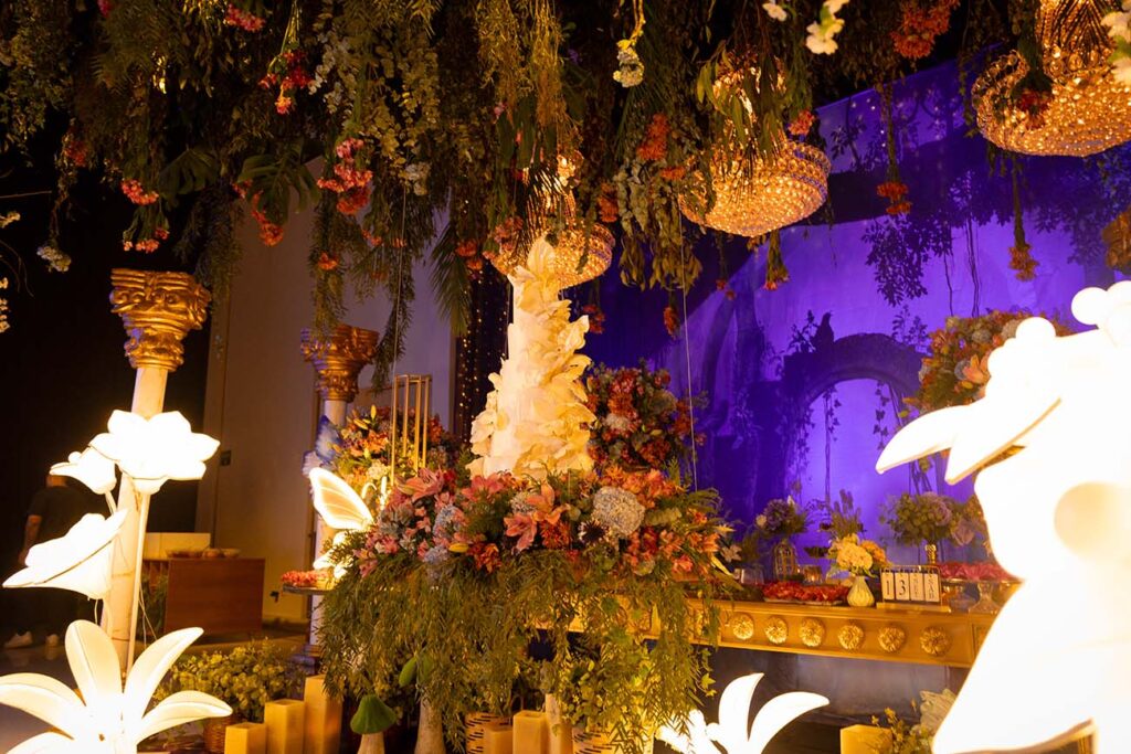 Mesa do bolo decorada com flores suspensas e iluminação em roxo