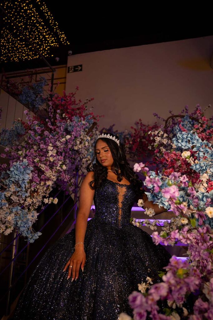 Debutante em vestido roxo sentada entre os arranjos de flores