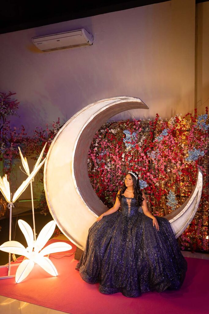 Debutante em vestido roxo sentada diante da lua decorativa iluminada