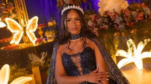 Debutante em vestido roxo com capa diante da decoração iluminada