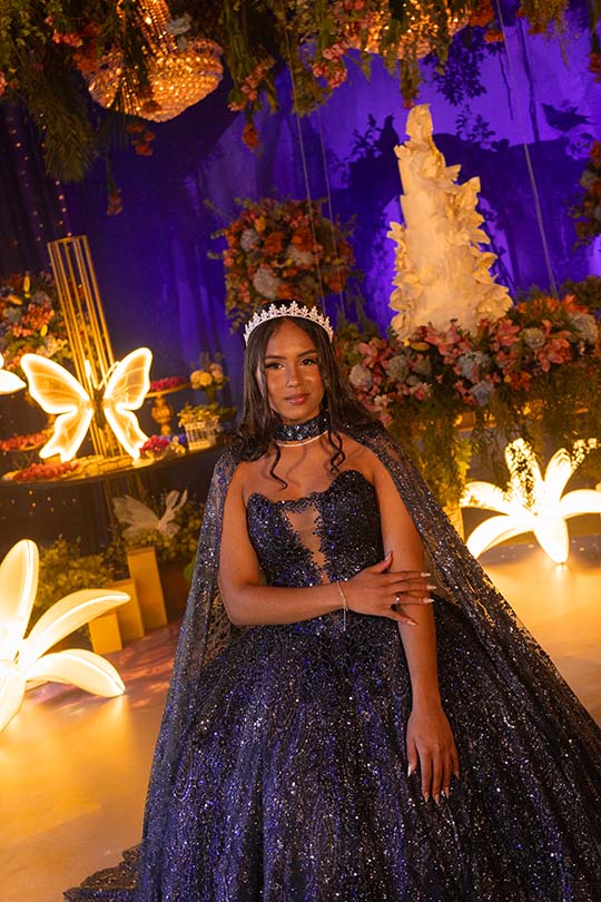 Debutante em vestido roxo com capa diante da decoração iluminada