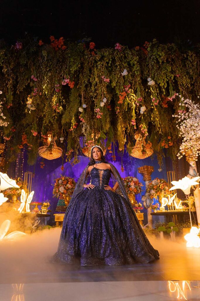 Debutante em vestido roxo no centro do cenário com flores suspensas