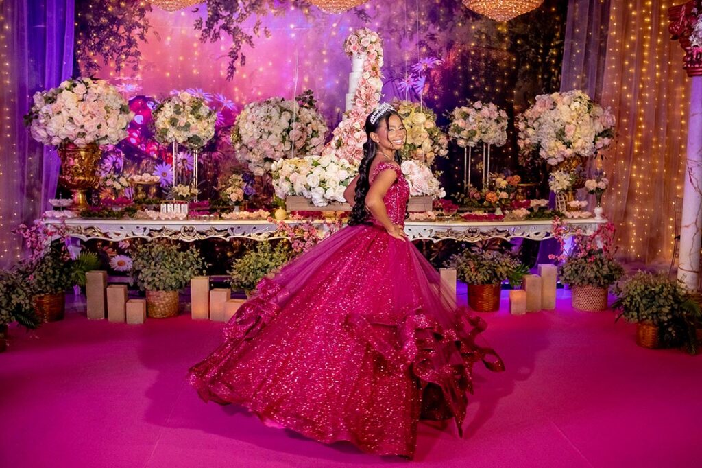 Debutante em vestido pink diante da mesa do bolo decorada com flores