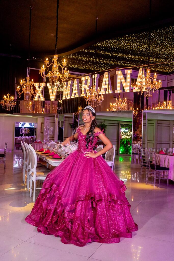 Debutante em vestido pink diante do letreiro luminoso com seu nome