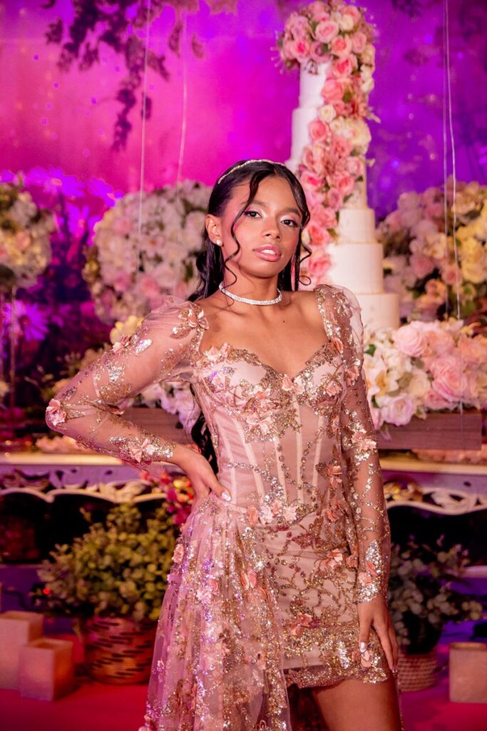 Debutante no segundo look dourado diante da decoração da festa