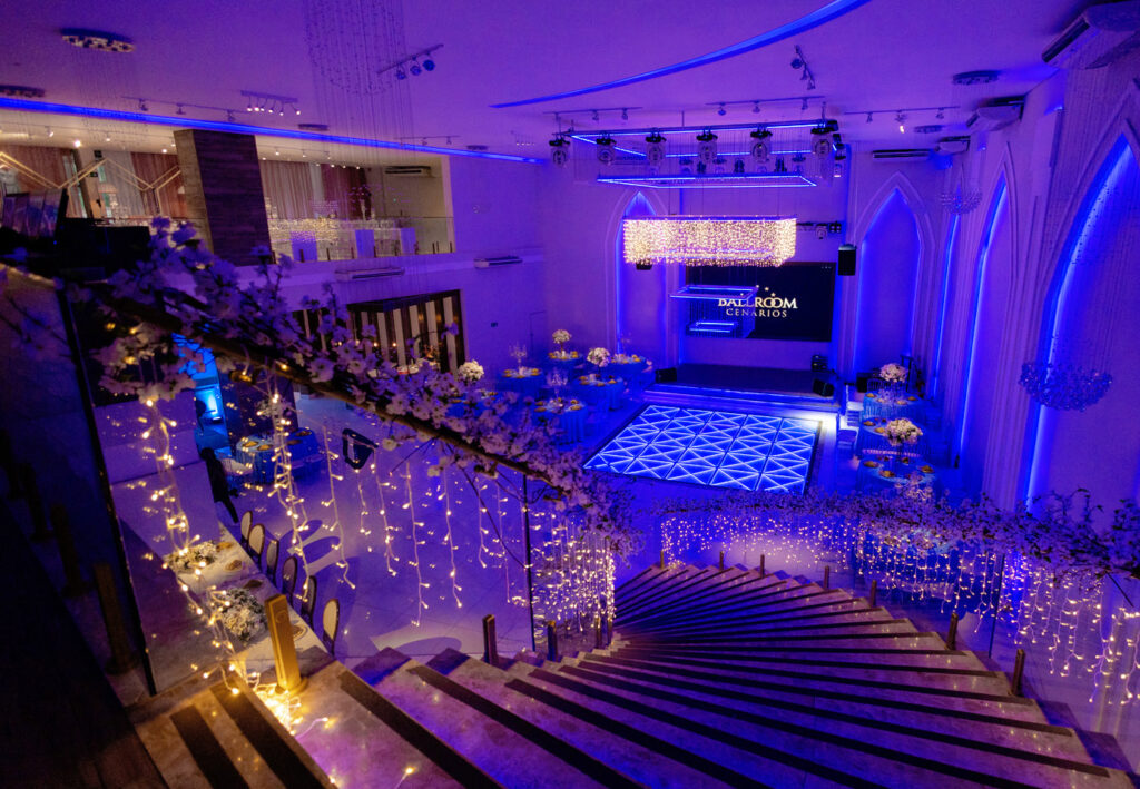 Salão iluminado em azul com pista central e decoração em flores