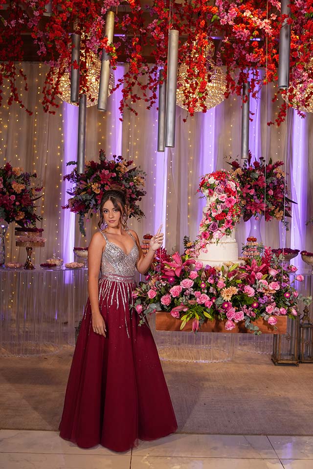 Debutante em vestido vinho ao lado da mesa do bolo