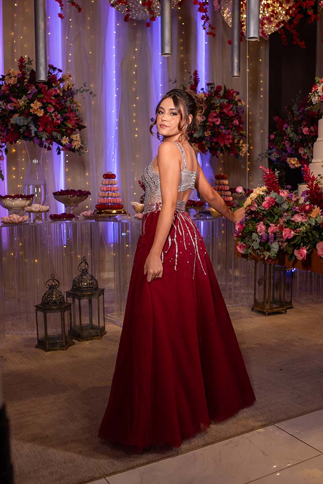 Debutante em vestido vinho de costas diante da mesa do bolo