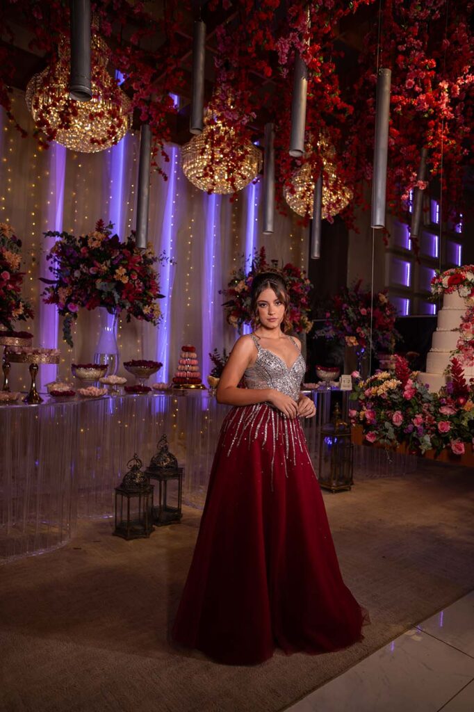 Debutante em vestido vinho diante dos arranjos de flores vermelhas