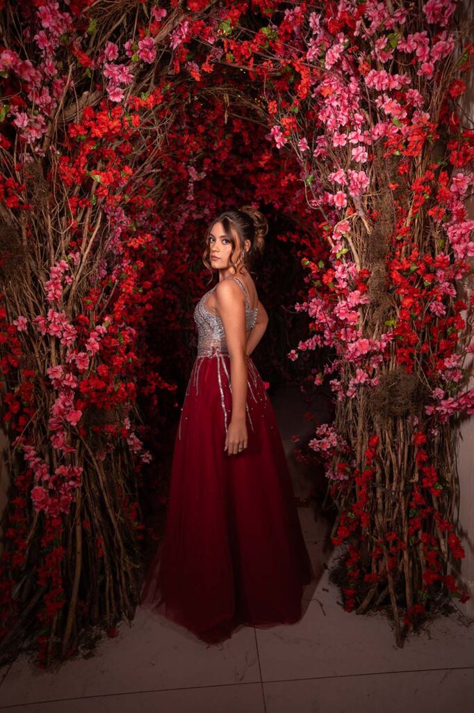 Debutante em vestido vinho emoldurada por galhos e flores vermelhas