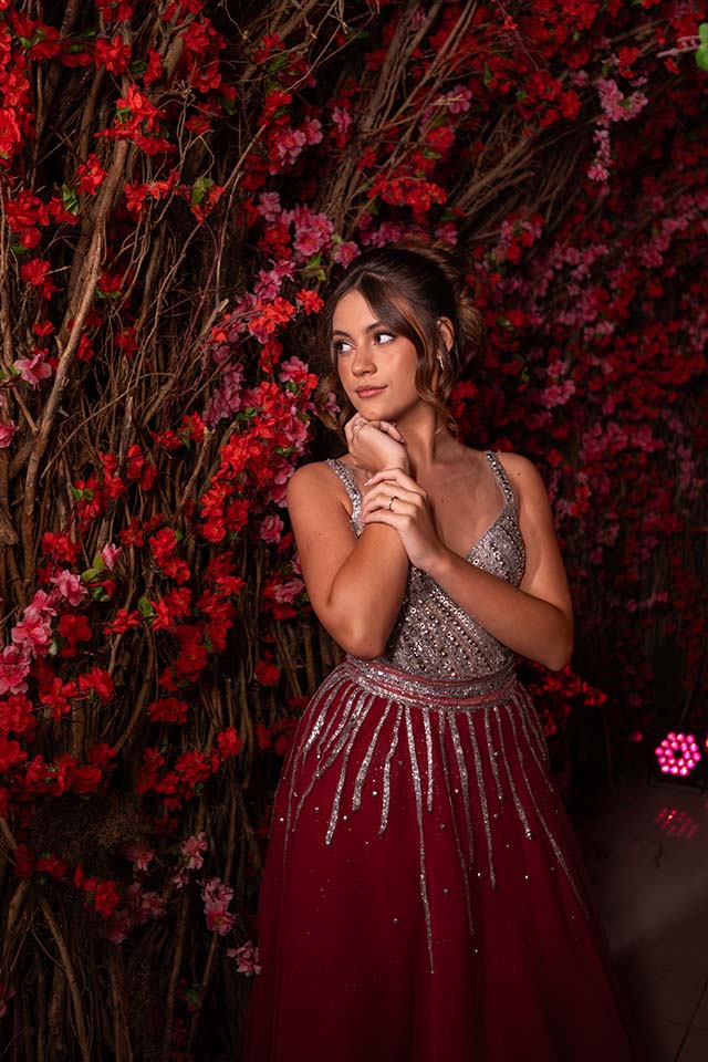 Debutante em vestido vinho entre os galhos floridos do cenário