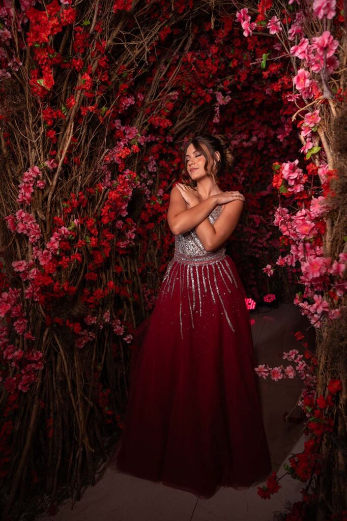 Debutante em vestido vinho diante da parede de flores vermelhas