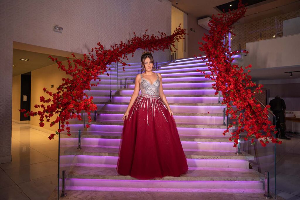 Debutante em vestido vinho na escadaria iluminada com arco de flores