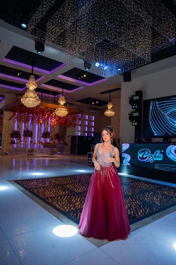 Debutante em vestido vinho na pista iluminada do salão