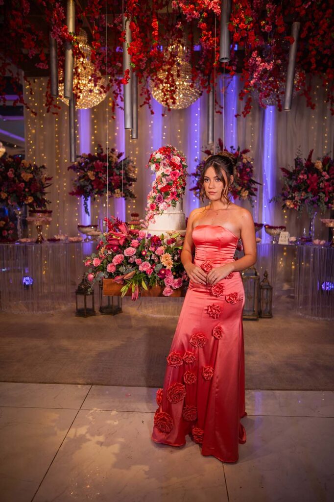 Debutante no segundo look coral ao lado da mesa do bolo