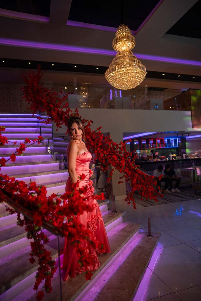 Debutante no segundo look coral diante da escadaria iluminada