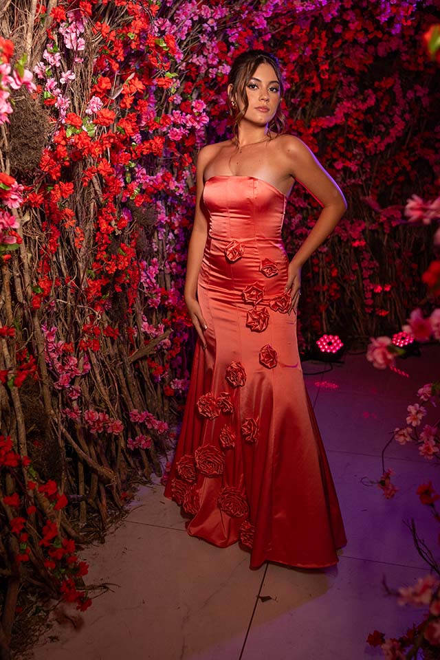 Debutante no segundo look coral entre as flores vermelhas suspensas
