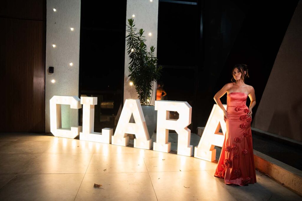 Debutante no segundo look coral ao lado do letreiro luminoso com seu nome