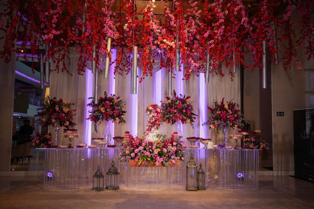 Mesa do bolo decorada com flores vermelhas suspensas e lanternas