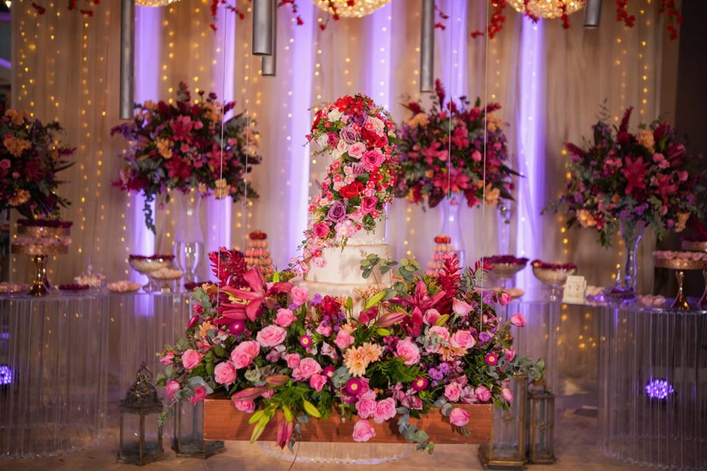 Bolo de 15 anos em branco cercado por arranjos de flores vermelhas e rosa