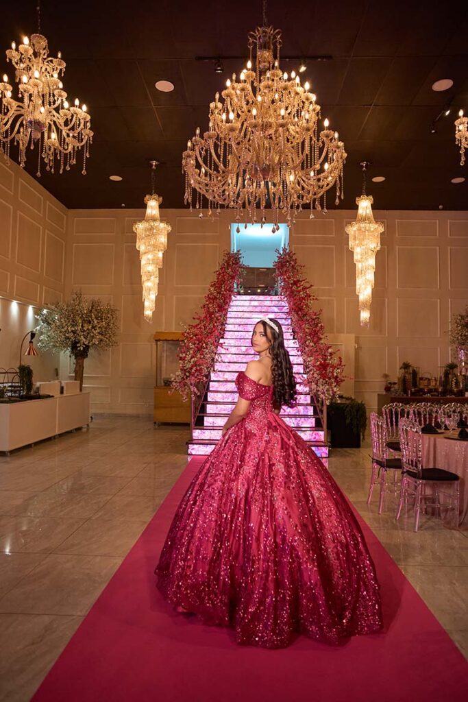 Debutante em vestido pink diante da escadaria e dos lustres
