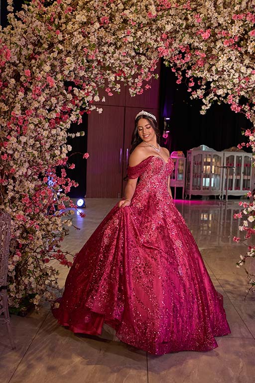 Debutante em vestido pink sob o arco de flores da entrada