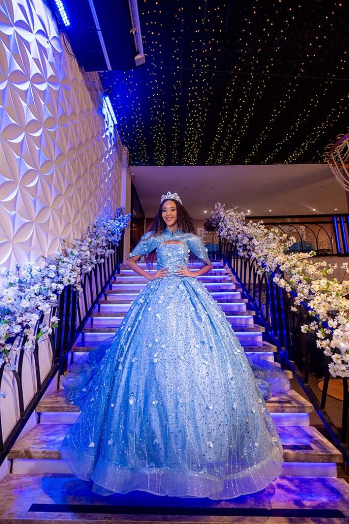 Debutante em vestido azul na escadaria decorada com flores