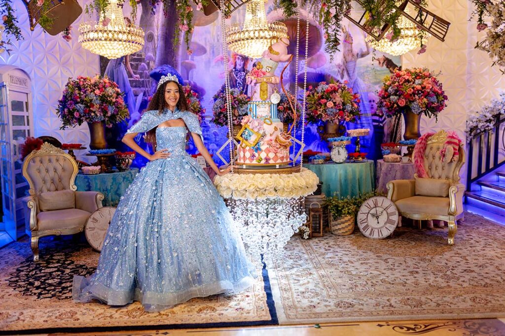 Debutante em vestido azul diante da mesa do bolo temática