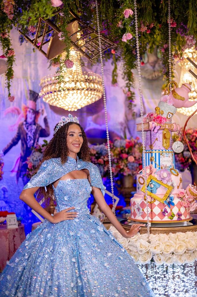 Debutante em vestido azul ao lado do bolo com relógios e cartas