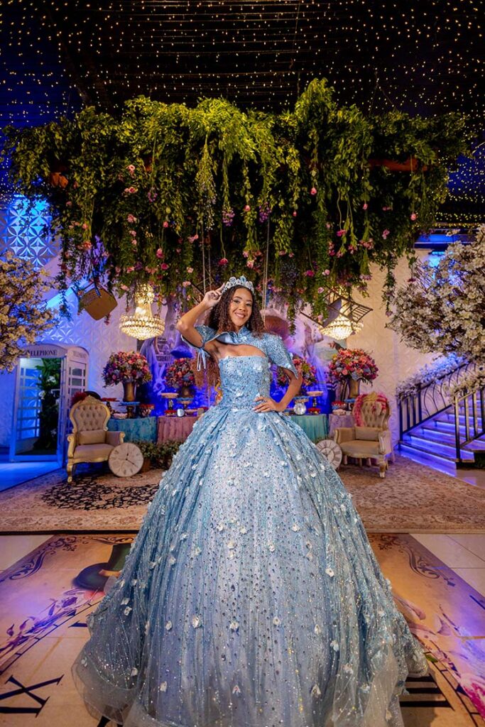 Debutante em vestido azul sob a vegetação e os lustres de cristal