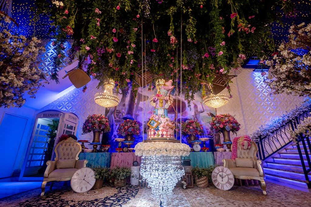 Mesa do bolo com lustres de cristal, flores e vegetação suspensa