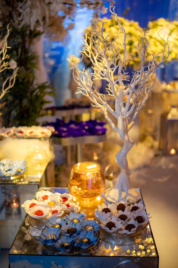 Mesa de doces com árvore decorativa branca e arranjos de flores