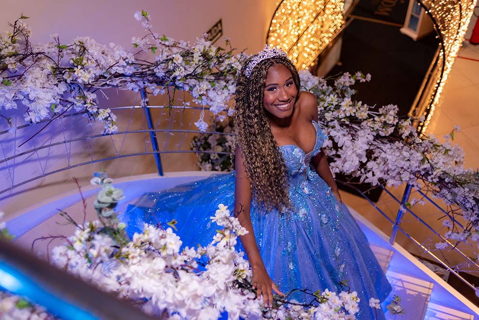 Debutante em vestido azul sentada na borda da fonte decorada com flores