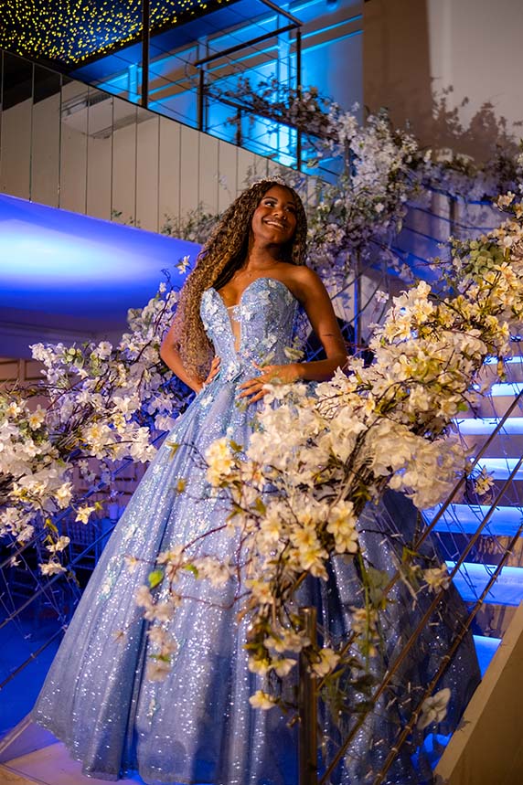 Debutante em vestido azul na escadaria decorada com flores