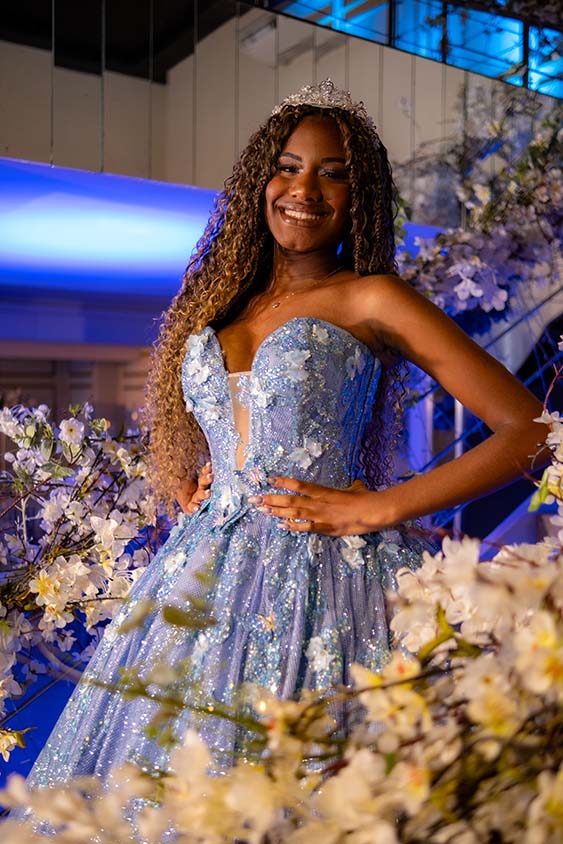 Debutante em vestido azul diante da parede de flores brancas
