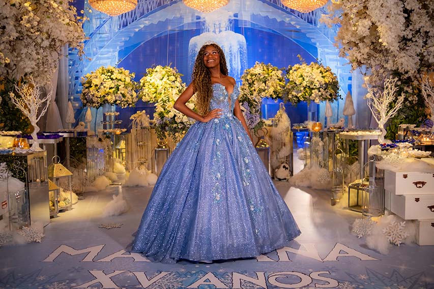 Debutante em vestido azul diante do arco iluminado e das árvores brancas