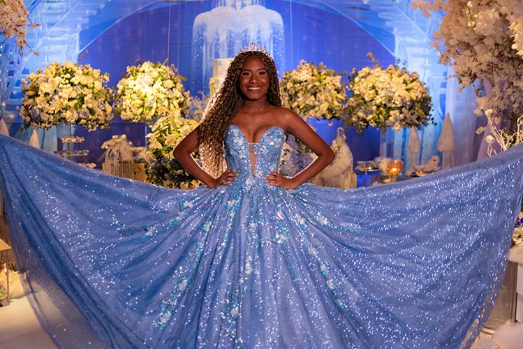 Debutante abre a saia do vestido azul diante do cenário iluminado