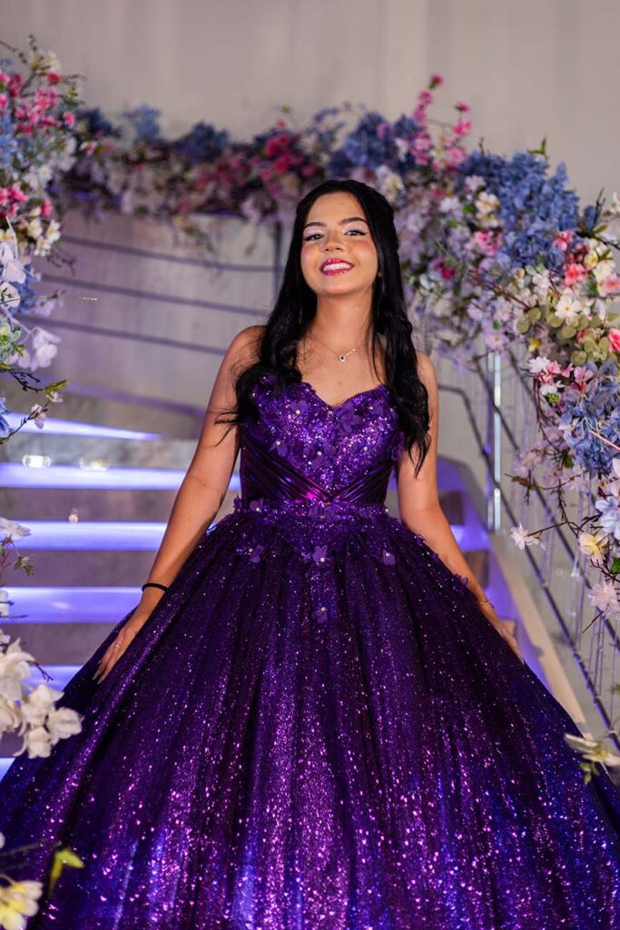Victoria em vestido roxo diante da escadaria decorada com flores
