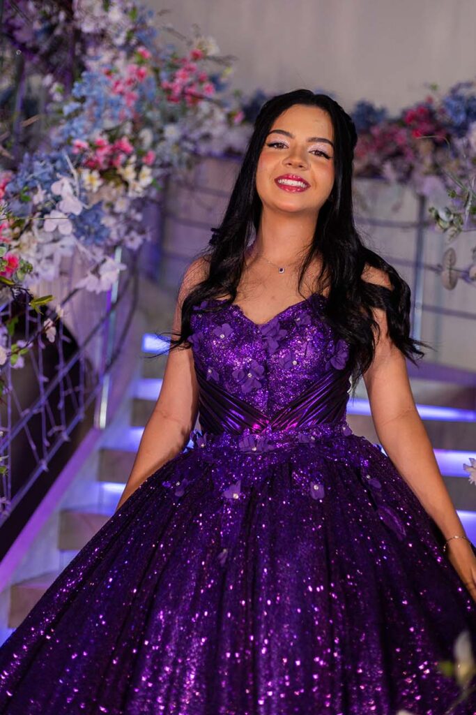 Debutante em vestido roxo ao pé da escadaria iluminada
