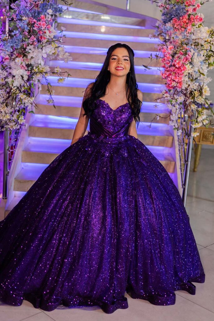 Debutante em vestido roxo na escadaria decorada com flores