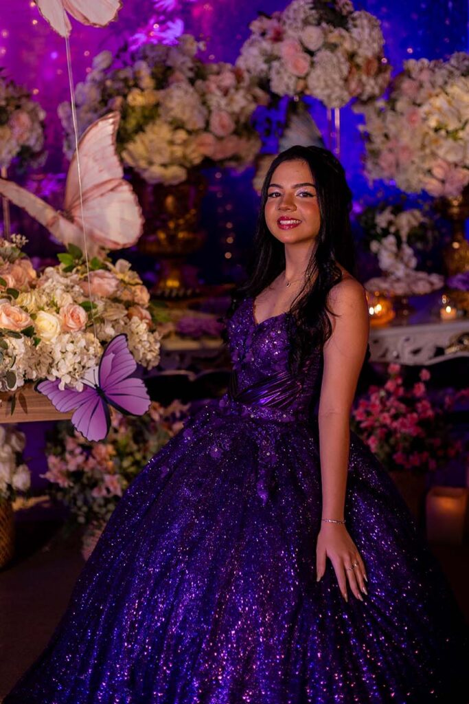 Debutante em vestido roxo diante dos arranjos de flores brancas
