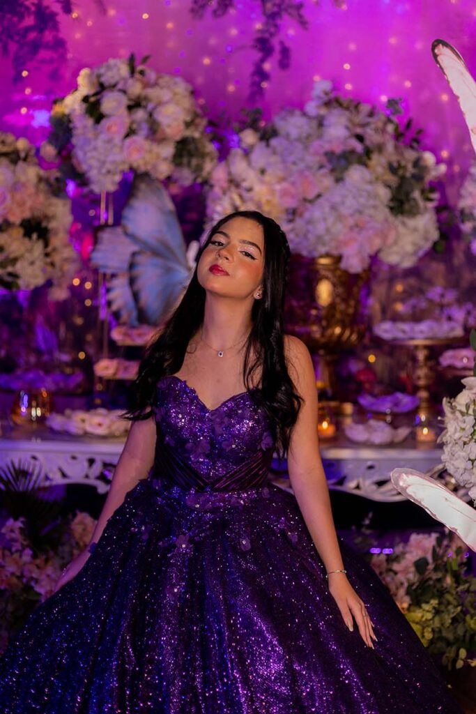 Debutante em vestido roxo diante da mesa do bolo iluminada